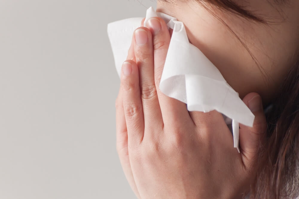 アレルギーで鼻をかむ女性のイメージ写真