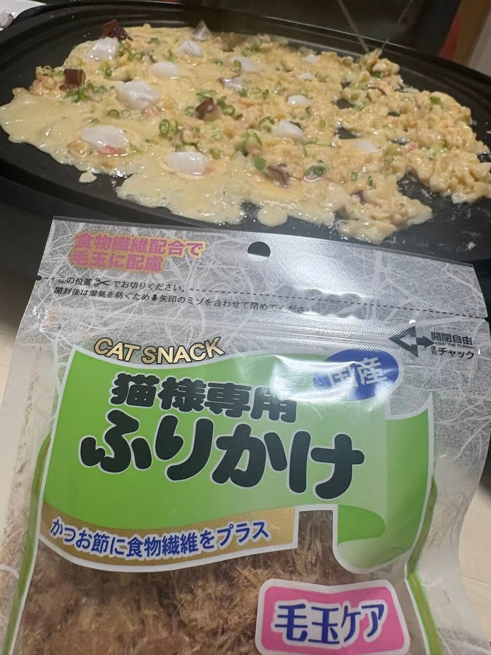 調理中のたこ焼きの前に置かれた猫用ふりかけのパッケージ